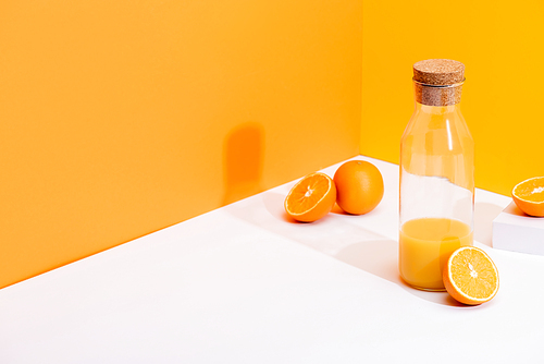 fresh orange juice in glass bottle near ripe oranges on white surface on orange background