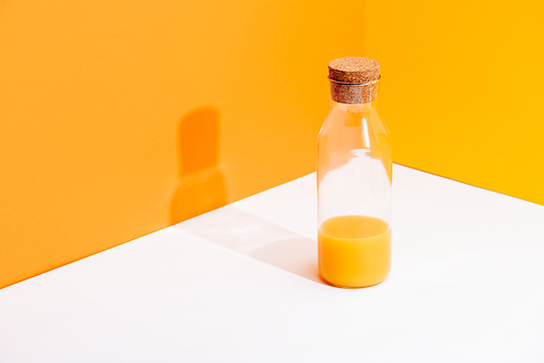 fresh orange juice in glass bottle on white surface on orange background