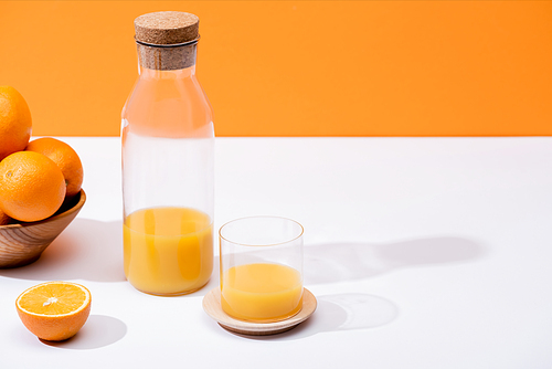 fresh orange juice in glass and bottle near oranges in wooden bowl on white surface isolated on orange