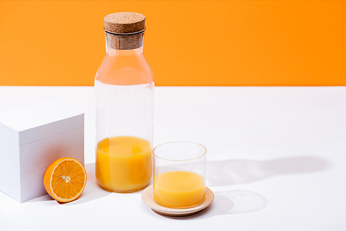 fresh orange juice in glass and bottle near ripe orange half on white surface isolated on orange