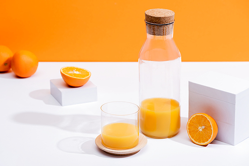 fresh orange juice in glass and bottle near ripe oranges on white surface isolated on orange