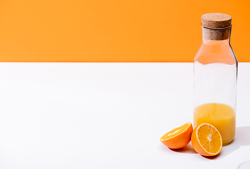 fresh orange juice in bottle near ripe orange halves on white surface isolated on orange