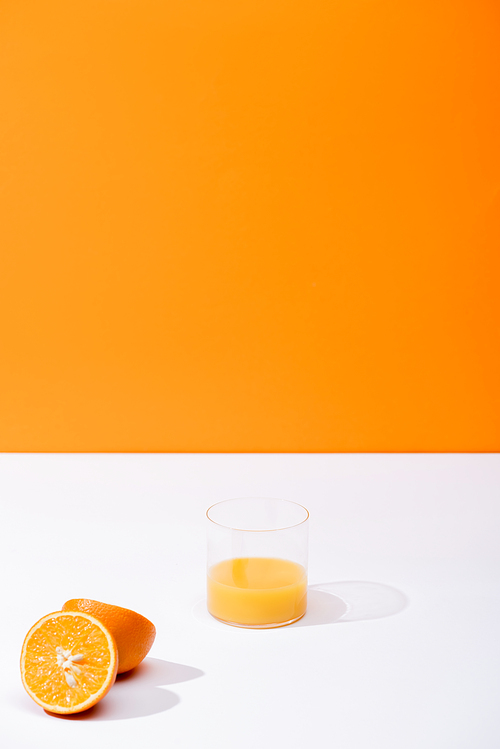 fresh orange juice in glass near ripe oranges on white surface isolated on orange