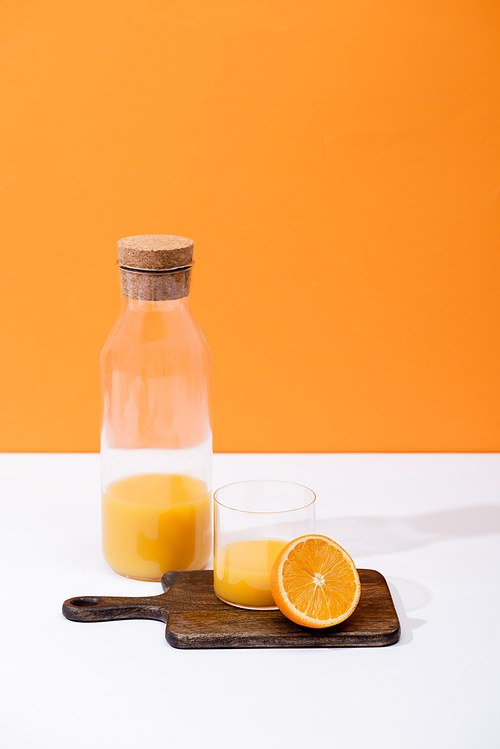 fresh orange juice in glass and bottle near cut fruit on wooden cutting board on white surface isolated on orange