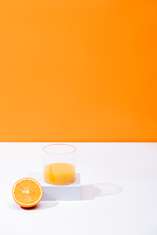 fresh orange juice in glass near cut fruit on white surface isolated on orange