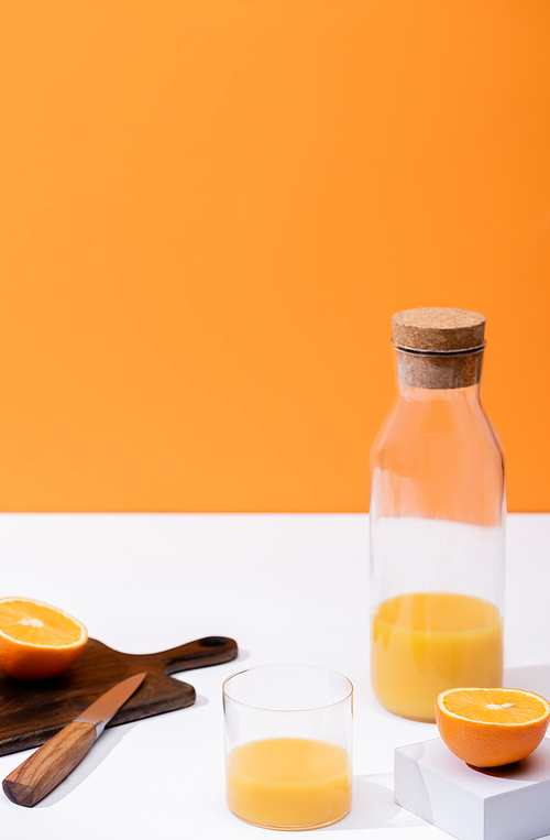fresh orange juice in glass and bottle near cut fruit on wooden cutting board with knife on white surface isolated on orange