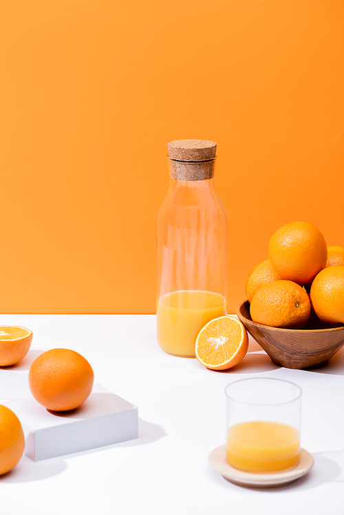 fresh orange juice in glass and bottle near oranges in bowl on white surface isolated on orange