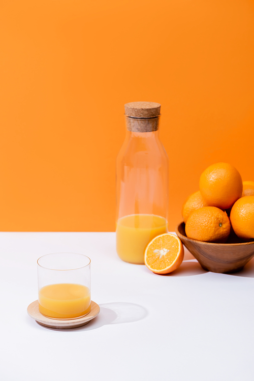 fresh orange juice in glass and bottle near oranges in bowl on white surface isolated on orange