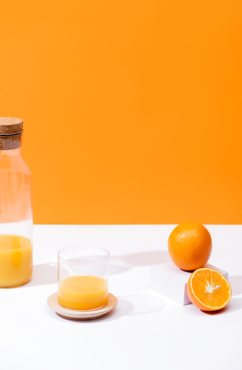 fresh orange juice in glass and bottle near oranges on white surface isolated on orange