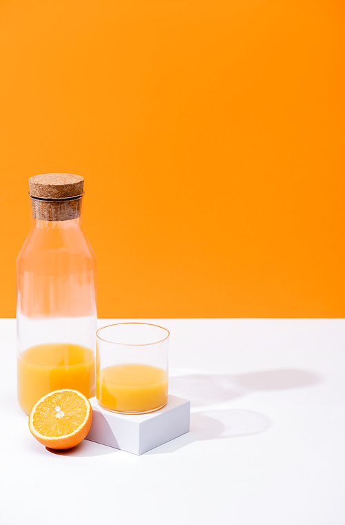 fresh orange juice in glass and bottle near cut fruit on white surface isolated on orange