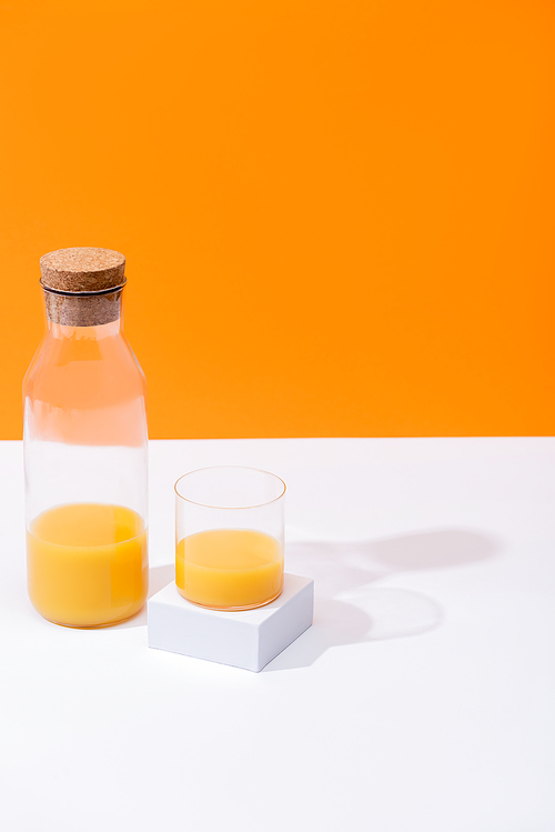 fresh orange juice in glass and bottle on white surface isolated on orange