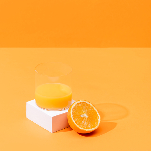 fresh orange juice in glass near half of orange and white cube isolated on orange