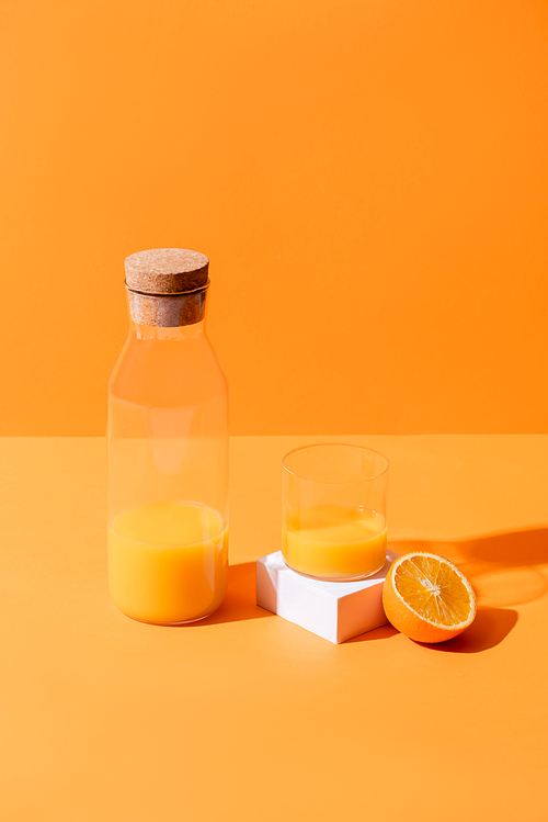 fresh orange juice in glass and bottle near half of orange and white cube isolated on orange