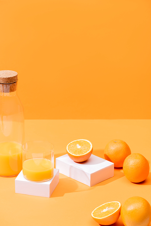 fresh orange juice in glass and bottle near ripe oranges and white cubes isolated on orange