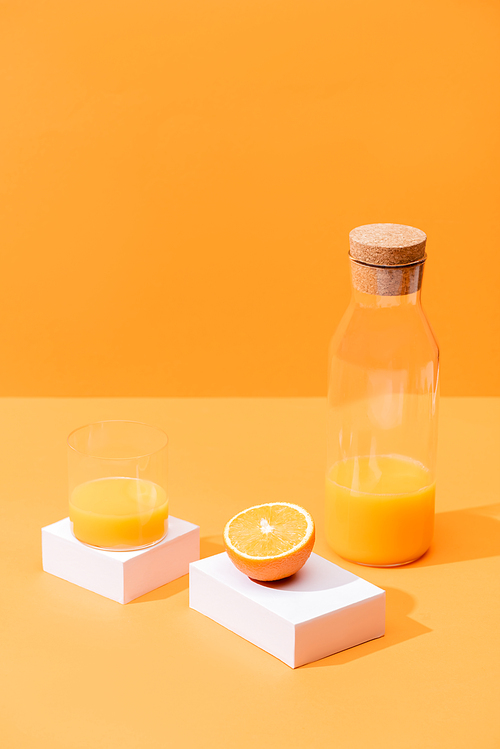 fresh orange juice in glass and bottle near cut orange and white cubes isolated on orange