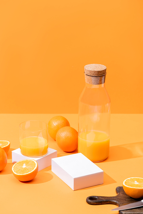 fresh orange juice in glass and bottle near ripe oranges, wooden cutting board with knife isolated on orange