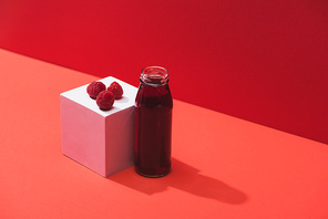 fresh berry juice in glass bottle near ripe raspberries on cube on red background