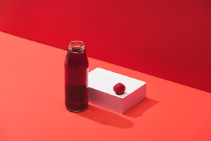 fresh berry juice in glass bottle near ripe raspberry on cube on red background