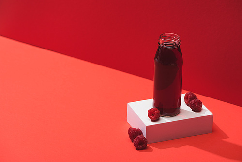 fresh berry juice in glass bottle near ripe raspberries on cube on red background