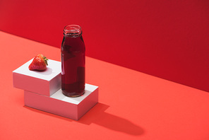 fresh berry juice in glass bottle near ripe strawberry on cubes on red background