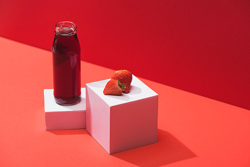 fresh berry juice in glass bottle near ripe strawberry on cubes on red background
