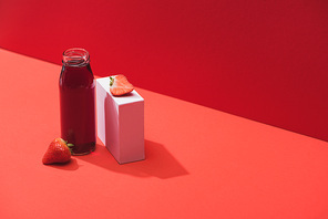 fresh berry juice in glass bottle near ripe strawberries on cube on red background