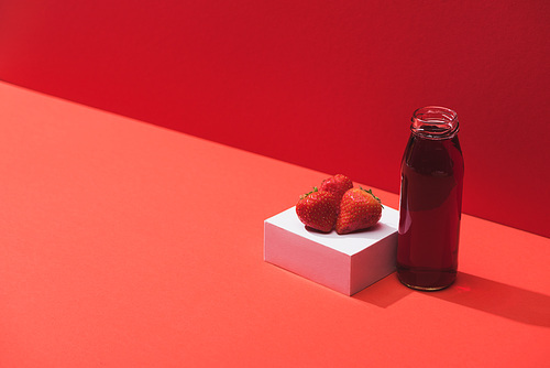 fresh berry juice in glass bottle near ripe strawberries on cube on red background