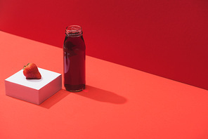 fresh berry juice in glass bottle near ripe strawberry on cube on red background