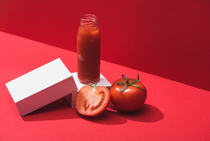 fresh vegetable juice in glass bottle and ripe tomatoes on cubes on red background