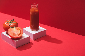 fresh vegetable juice in glass bottle and ripe tomatoes on cubes on red background