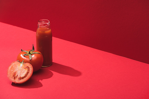 fresh vegetable juice in glass bottle and ripe tomatoes on red background
