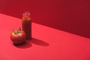 fresh vegetable juice in glass bottle and ripe tomato on red background