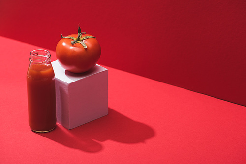 fresh vegetable juice in glass bottle and ripe tomato on cube on red background