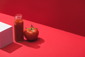 fresh vegetable juice in glass bottle near ripe tomato and cube on red background