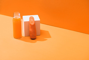 fresh juice in glass bottle near ripe carrot and cube on orange background