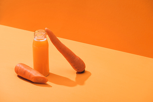 fresh juice in glass bottle near ripe carrots on orange background