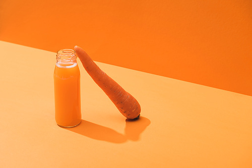 fresh juice in glass bottle near ripe carrot on orange background