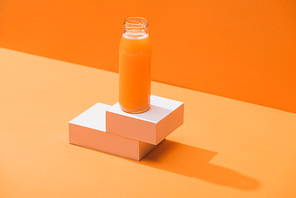 fresh carrot juice in glass bottle on cubes on orange background