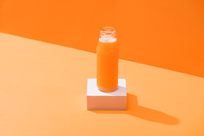 fresh carrot juice in glass bottle on cube on orange background
