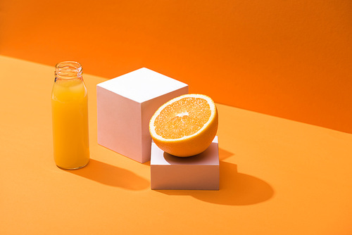 fresh juice in glass bottle near orange half and white cubes on orange background