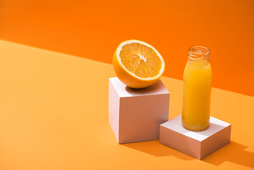 fresh juice in glass bottle near orange half and white cubes on orange background