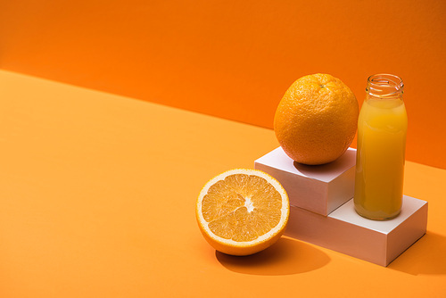 fresh juice in glass bottle near oranges and white cubes on orange background