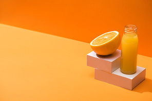 fresh juice in glass bottle near orange half and white cubes on orange background