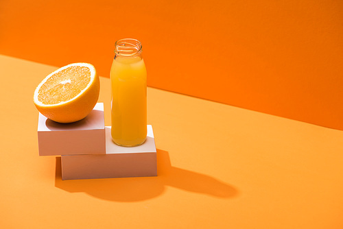 fresh juice in glass bottle near orange half and white cubes on orange background
