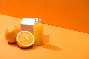 fresh juice in glass bottle near oranges and white cube on orange background