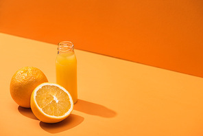 fresh juice in glass bottle near oranges on orange background