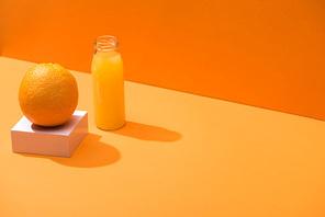 fresh juice in glass bottle near whole orange and white cube on orange background