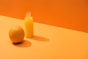 fresh juice in glass bottle near whole orange on orange background