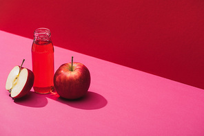fresh juice in bottle near apples on red and pink background