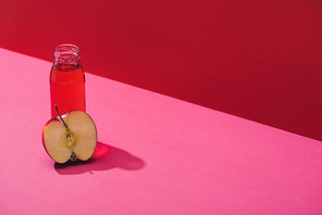 fresh juice in bottle near apple half on red and pink background